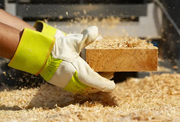 Güvenlik eldivenli bir insanın, bir parça 2x4 'ü sanayi zımpara makinesiyle kurtarırken çekilmiş fotoğrafı..