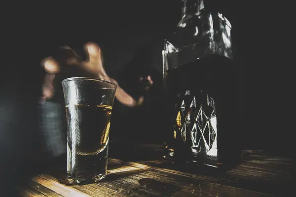 Yalnız, depresif, kukuletalı bir adamın portresi. Tahta bir barın üstünde viski içmeye çalışıyor..