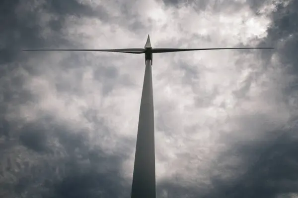Uzun rüzgar türbinleri dramatik ve fırtınalı bir gökyüzüne karşı duruyor.