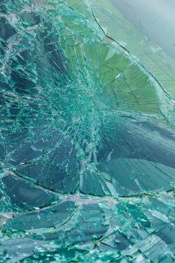 Karmaşık çatlaklarla parçalanmış yeşil güvenlik camlarının yakın çekimi. Kırık cam desenleri radyal çatlak çizgilerini gösteriyor..