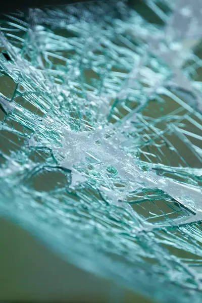 Radyal çatlaklarla parçalanmış güvenlik camının detaylı görüntüsü. Hasarlı araba camında çatlaklar ve kıymıklar var..