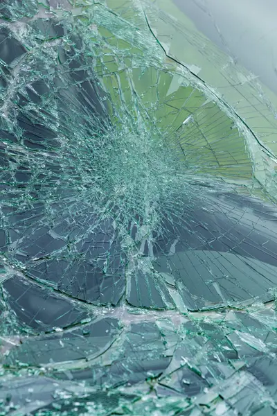 Karmaşık çatlaklarla parçalanmış yeşil güvenlik camlarının yakın çekimi. Kırık cam desenleri radyal çatlak çizgilerini gösteriyor..
