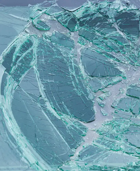 Kırık cam yüzey ve keskin yeşil parçalar. Çatlak ön cam detayı güvenlik camının yapısını gösteriyor..