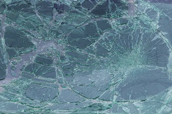Karmaşık çatlaklarla parçalanmış yeşil güvenlik camlarının yakın çekimi. Kırık cam desenleri radyal çatlak çizgilerini gösteriyor..