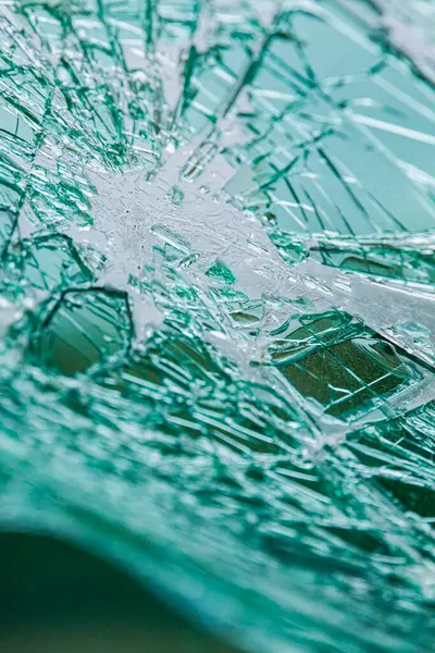 Kırık bir ön camda, ağımsı çatlaklar var. Çarpışmadan dolayı kırılan yeşil renkli güvenlik camı..