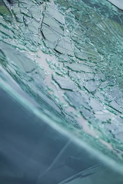 Arabanın ön camındaki kırık güvenlik camının detaylı görüntüsü. Kırık cam desenleri merkezi darbe noktasından yayılıyor..