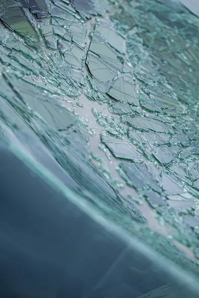 Kırık ön cam ve parlak çatlaklar. Hasarlı bir güvenlik camındaki örümcek ağı çatlaklarına yakın çekim.