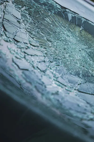 Arabanın ön camındaki kırık güvenlik camının detaylı görüntüsü. Kırık cam desenleri merkezi darbe noktasından yayılıyor..