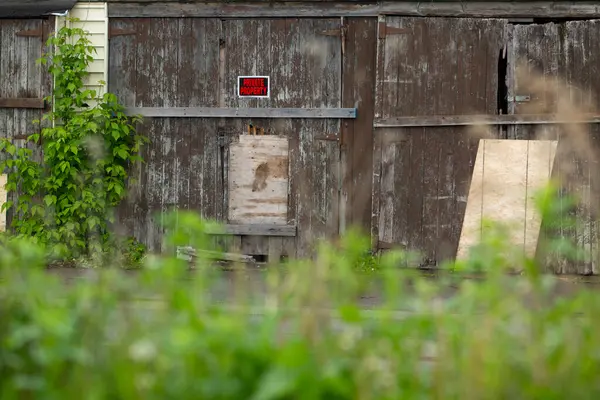 Yıpranmış ahır kapıları, izinsiz giriş ve aşırı büyümüş yeşillikler. Terk edilmiş bina kısmen binilmiş ve doğa tarafından geri alınmış..