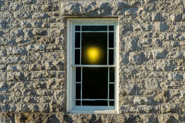 Taş bir duvarda sıcak bir ışıkla parlayan lekeli cam pencereler..