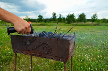 Gaz ocağını teneke kutuyla tutan ve ızgarada yangın çıkaran bir adamın yakın çekimi. Akşam bahçedeki yeşil çimlere karşı topun alevi. Erkeğin elleri ateş yakar..