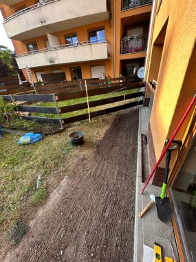 Bahçe düzenleme sahnesi, yerleşim yerinin yanında yeni hazırlanmış toprak, görünürde ahşap çit ve bahçe dekorasyonu araçları, açık hava yenileme çalışmalarını gösteriyor.