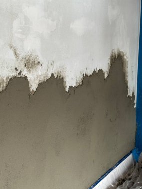 Duvara yeni uygulanan çimento sıva, ıslak ve kuru dokuların bir karışımını sergiliyor, ev yenileme ve inşaat çalışmalarındaki beceri ve beceriyi vurguluyor