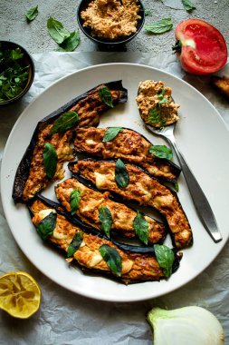 İçi süzme peynirle doldurulmuş patlıcan, doğranmış domates, soğan ve taze fesleğen yaprakları. Vejetaryen yemek tarifi. Sağlıklı beslenme. İtalyan yemeği. Gri arkaplan, üst görünüm. 