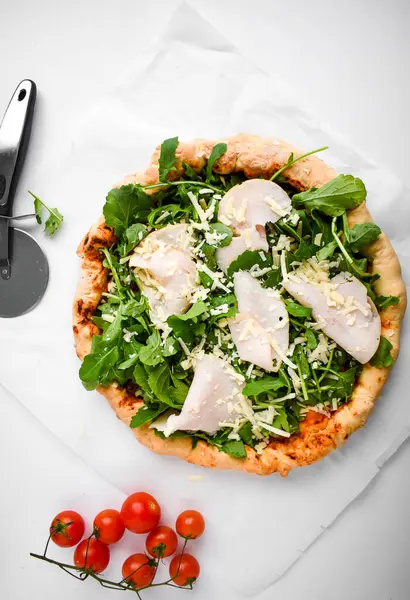 İtalyan pizzası, prosciutto, roka, parmesan peyniri, beyaz masada vişneli domates. Vejetaryen yemek tarifi. Sağlıklı beslenme. İtalyan mutfağı. Üst görünüm.