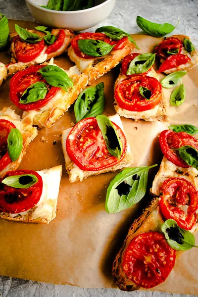 Lezzetli bruschetta, mozarella, domates ve fesleğen. İtalyan antipasti aperatifleri. Üst manzara, gri arkaplan. Geleneksel İtalyan atıştırması.