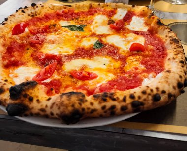 Domates sosu, mozzarella, vişneli domates ve fesleğenli taze Margherita pizzası. Taze pişmiş ve beyaz bir tabakta servis edilmiş..