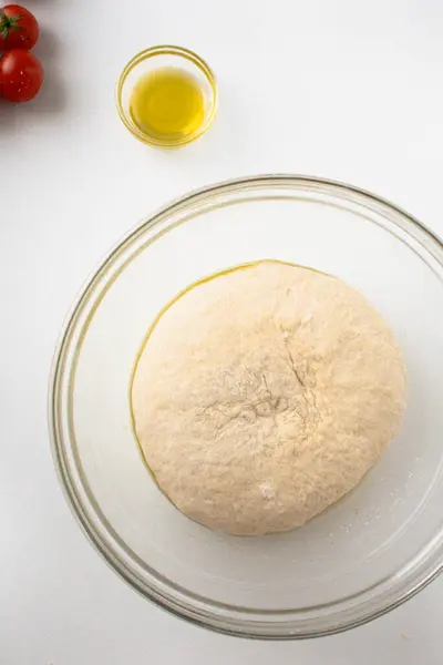 Çiğ maya hamuru dinleniyor ve plastik torbayla kaplı büyük bir cam kasede yükseliyor..