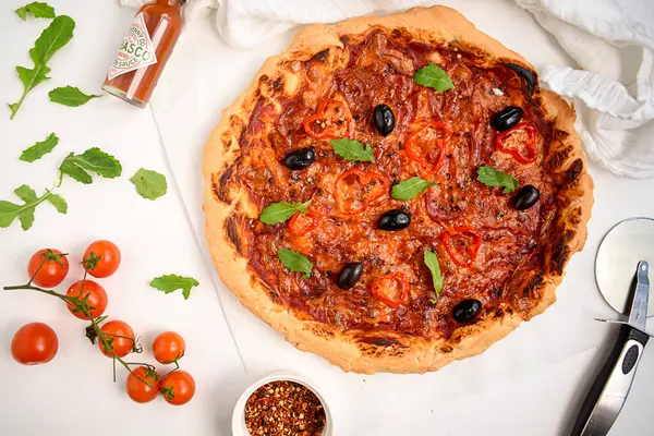 İtalyan pizzası beyaz masada, malzemelerle dolu.