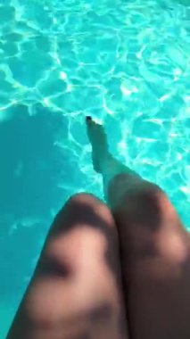  Beyaz kadın güneşleniyor ve ayaklarını yüzme havuzuna sokuyor. Seksi kadın yüzme havuzunun yanında oturup dinleniyor..