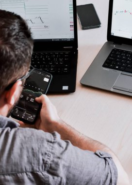 Genç bir iş adamı telefonunu kullanıyor, ofisinde çalışıyor.