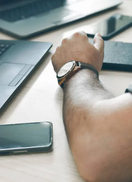 İnternette çalışmak için laptop, tablet ve telefon kullanırken saat takan bir adamın omzuna yakın çekim.