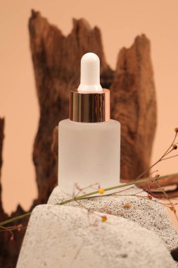 Serumlu kozmetik şişesi ve bej arka planda kuru yaprak..