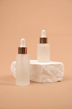 Açık bej arka planda iki şişe kozmetik şişesi olan iki beyaz serum ve krem. cilt bakımı, güzellik, vücut ve yüz kremi.