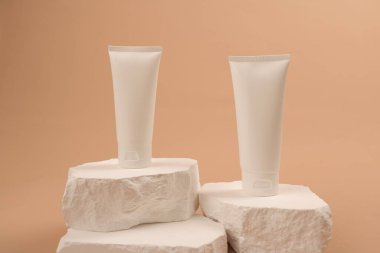 Beyaz podyumda bej arka planda iki kozmetik ürünü.