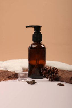 Bej arka planda bir şişe kozmetik krem ve kahverengi havlu..