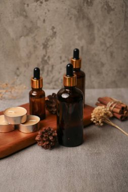 Farklı kozmetik ürünleri olan şişeler ve gri arka planda kuru yapraklar.