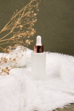 Beyaz mermer arka planda serum ve çiçeklerle dolu bir şişe.