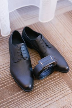 Siyah resmi erkek ayakkabıları ve çizgili kahverengi bir zemine siyah bir kemer.