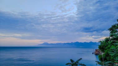 Uzakta deniz ve dağların olduğu manzara, mavi renk baskın gelir.