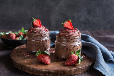 Delicious chocolate mousse topped with fresh and freeze-dried strawberries in glass jars clipart