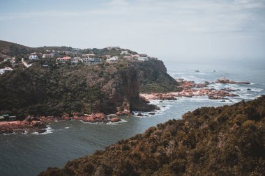 Bu çarpıcı fotoğraf, Güney Afrika kıyı şeridi boyunca uzanan manzaralı kayalıkları ve büyüleyici evleri çekiyor. Seyahat ve gayrimenkul meraklıları için mükemmel, deniz kenarında yaşamanın güzelliğini gözler önüne seriyor..