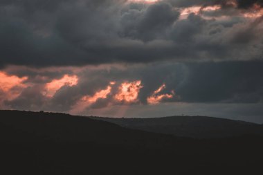 Bu dramatik fotoğraf, Güney Afrika tepeleri üzerinde fırtınalı bir günbatımını yakalar, ışık ve kara bulutların etkileşimini gösterir. Doğa, seyahat ve hava durumuyla ilgili içerik için mükemmel.