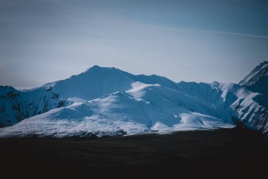 Taze karla kaplı Alaska dağlarının nefes kesici manzarası, yumuşak sabah ışığı yumuşak gölgeler bırakıyor. Doğanın saf güzelliğini ve sükunetini göstermek için mükemmel..