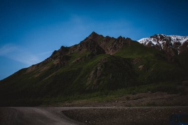 Alaska 'nın engebeli dağlarının büyüleyici güzelliğini parlak mavi gökyüzünün altında yakala. Bu çarpıcı manzara çekimi doğa, seyahat ve macera temalı projeler için idealdir..
