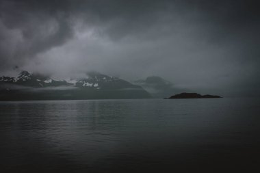 Sisli dağlarla çevrili bir Alaska gölünün karamsar ve sakin manzarası. Sis, doğa ve seyahat temaları için mükemmel gizemli ve sakin bir atmosfer yaratır..