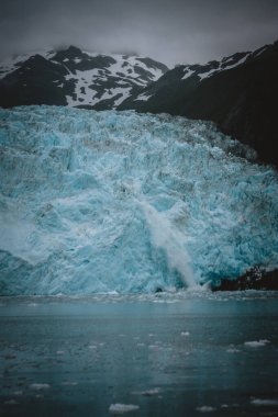 Büyük bir Alaska buzulunun engebeli bir dağ zeminine çarpıcı şekilde düşüşüne tanık olun. Doğa, macera ve iklim değişikliği farkındalığı konuları için mükemmel..