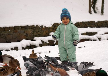 Kışın güvercinler ve ördekler arasında parkta gülümseyen tatlı bir oğlan.