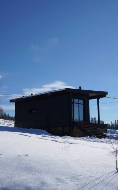 Kışın mavi gökyüzü ile dağda tahta siyah küçük bir ev.