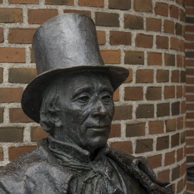 Yazar H. C. Andersen 'in gülümseyerek bronz heykeli, 19 Nisan 2024' te Danimarka 'nın Odense şehrinde tuğla bir duvara karşı durmaktadır.