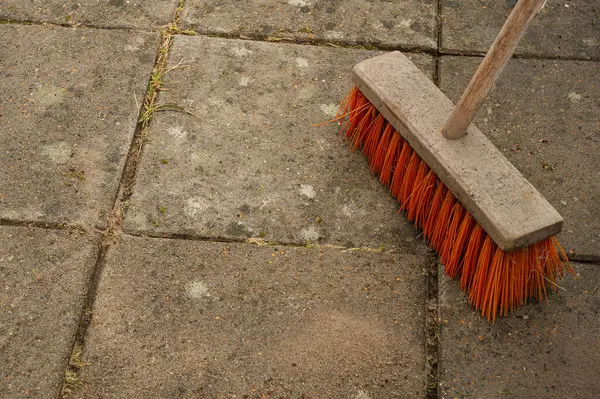 Kırmızı piasava süpürgesi yeni yıkanmış bahçe fayanslarının üzerinde duruyor.