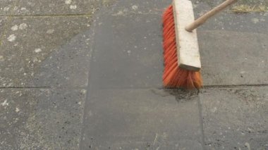 Kırmızı piasava süpürgesi yeni yıkanmış bahçe fayanslarının üzerinde duruyor.