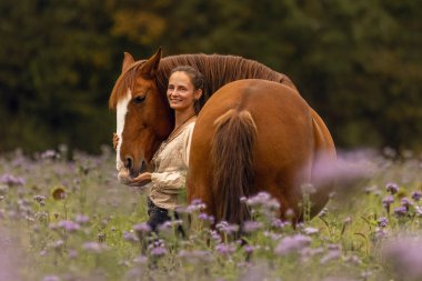 Bir kadın ve Lusitano atı sonbaharda bir kır çiçeğinin çayırında sarılıp kaynaşıyorlar.