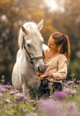 Genç bir kadın, sonbaharda açık havada yabani bir çiçek tarlasında beyaz İspanyol boynuzuyla sarılıp etkileşime geçiyor.