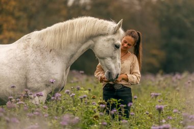 Genç bir kadın, sonbaharda açık havada yabani bir çiçek tarlasında beyaz İspanyol boynuzuyla sarılıp etkileşime geçiyor.