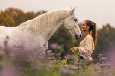 Genç bir kadın, sonbaharda açık havada yabani bir çiçek tarlasında beyaz İspanyol boynuzuyla sarılıp etkileşime geçiyor.